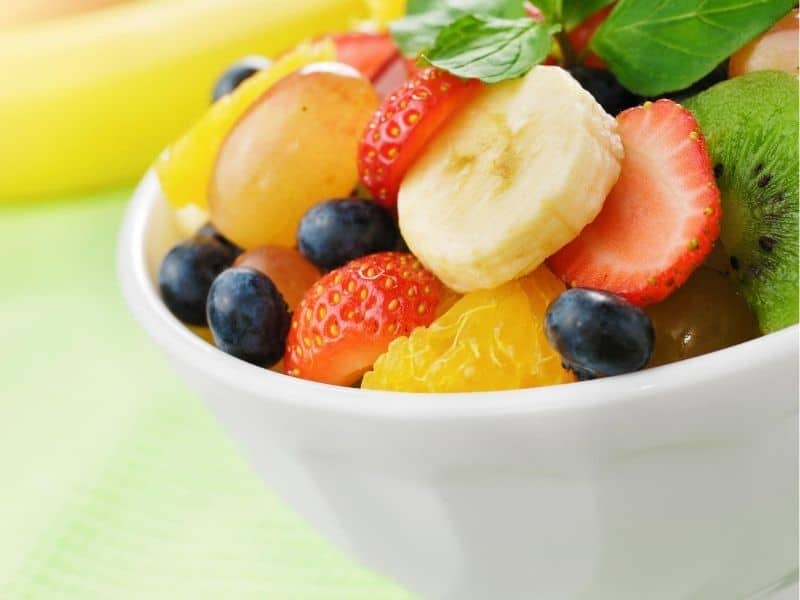 A bowl of sweet fruits: banana, strawberries, grapes, and blueberries