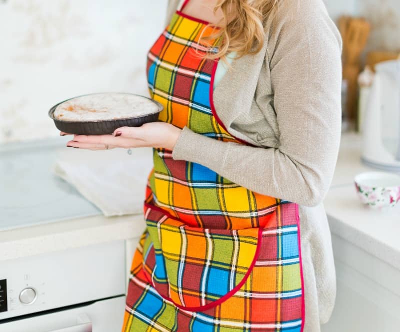 Woman pulling pie from oven, wearing a beautiful Thaksgiving apron 